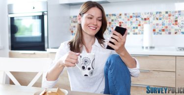 Woman in kitchen looking at surveys on her phone