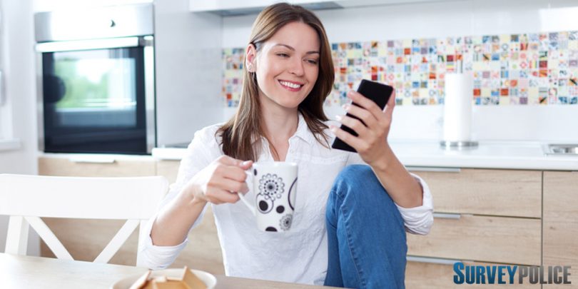 Woman in kitchen looking at surveys on her phone