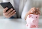Woman holding phone with piggy bank on table