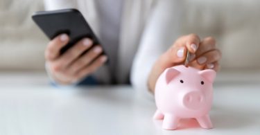 Woman holding phone with piggy bank on table