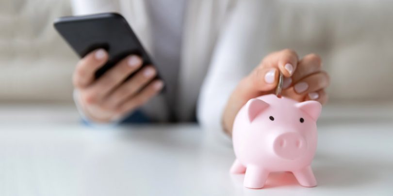 Woman holding phone with piggy bank on table