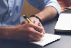 Man writing tips next to laptop