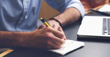 Man writing tips next to laptop