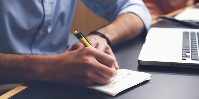 Man writing tips next to laptop