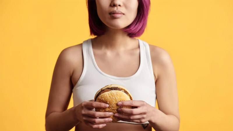 Woman holding hamburger in front of yellow background